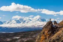 Турист, стоящий на вершине скалы, обнаженной на Донелли-Доум, любуясь видом на гору Моффит и Аляскинский хребет; Аляска, Соединенные Штаты Америки — стоковое фото