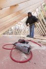 Close-up of a nail gun with a carpenter using measuring tape in the background — Stock Photo