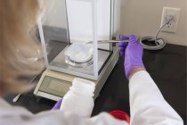 Scientifique de laboratoire ajoutant une petite quantité de réactif solide à un récipient sur une échelle — Photo de stock