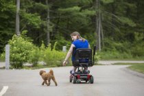 Mujer joven con parálisis cerebral jugando con su perro mientras está sentada en su scooter - foto de stock