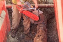 Trabalhador da construção usando serra para cortar através de tubulação de água velha — Fotografia de Stock