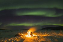 Staying warm beside a campfire on the Delta River while watching the aurora borealis on a frigid night; Alaska, United States of America — Stock Photo