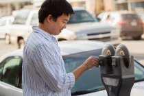 Chinese man putting money in a parking meter — Stock Photo