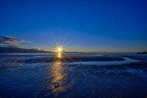 Puesta de sol sobre la bahía de Tasman, iluminando la arena mojada en la orilla de Pohara Beach; Nelson, Isla Sur, Nueva Zelanda - foto de stock