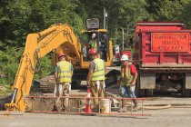 Trabalhadores da construção civil assistindo escavadoras cavando buraco no projeto watermain — Fotografia de Stock