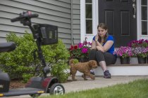 Mujer joven con parálisis cerebral jugando con su perro mientras su scooter está allí - foto de stock