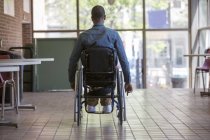 Человек, у которого был менингит позвоночника в инвалидной коляске, направляющийся к лифту по лестнице в офис — стоковое фото