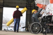 Maintenance supervisor with a spinal cord injury in utility garage and loading new truck with supplies one man carrying hole shielding — Stock Photo