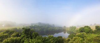 Arco iris y niebla temprano en la mañana sobre un estanque interior - foto de stock