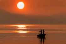 Силуетанги стоять на човні й ловлять лосося на заході сонця; Джуно, Аляска, Сполучені Штати Америки. — стокове фото