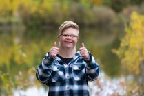A young man with Down Syndrome giving a thumbs up in a city park on a warm fall evening: Edmonton, Alberta, Canada — Stock Photo