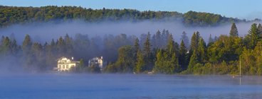 Mist laying over Lac a la Truite at dawn with low clouds hanging over the forest along the shoreline; Quebec, Canada — Fotografia de Stock