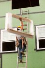 Hispanic carpenter climbing ladder with new window frame — Stock Photo