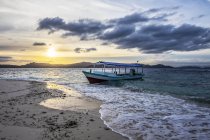 Barco en la playa al atardecer, Pulau Kelelawar (Bat Island); Papúa Occidental, Indonesia - foto de stock