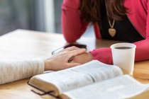 A mature Christian woman mentoring and praying with a young woman during a bible study in a coffee shop at a church: Edmonton, Alberta, Canada — Stock Photo