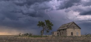 Un éclair à fourche descend d'un faible orage près d'un bâtiment abandonné ; Guymon, Oklahoma, États-Unis d'Amérique — Photo de stock