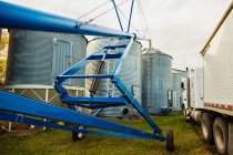 An auger assembly and grain truck parked beside silos in a farmyard; Legal, Alberta, Canada — Stock Photo