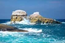 El agua azul del Mediterráneo salpica contra formaciones rocosas blancas a lo largo de la costa de una isla griega; Milos, Grecia - foto de stock