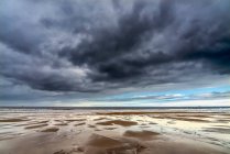 Nubes de tormenta oscura sobre el océano Atlántico con playa de arena mojada en primer plano; South Shields, Tyne and Wear, Inglaterra - foto de stock
