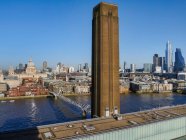Schornstein des Tate Modern Art Museum und die Millennium Bridge überqueren die Themse mit einem Stadtbild von London; London, England — Stockfoto