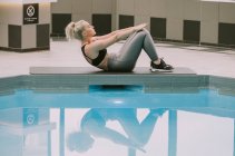 Donna che lavora su un tappeto facendo un esercizio addominale accanto a una piscina; Wellington, Nuova Zelanda — Foto stock