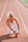 Woman kneeling to tie her running shoe to prepare for running on a track; Wellington, New Zealand — Stock Photo