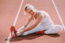 Donna seduta a allungare i muscoli delle gambe per prepararsi a correre su una pista; Wellington, Nuova Zelanda — Foto stock