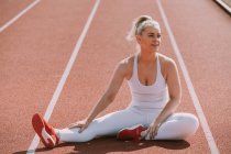 Donna seduta a allungare i muscoli delle gambe per prepararsi a correre su una pista; Wellington, Nuova Zelanda — Foto stock