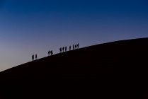 Siluetas de turistas escalando la Duna 45 al atardecer, Sossusvlei, desierto de Namib; Namibia - foto de stock