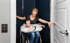 Eine querschnittsgelähmte Mutter hält ihr Baby auf dem Schoß, während sie mit ihrem Rollstuhl in ihren Fahrstuhl steigt: Edmonton, Alberta, Kanada — Stockfoto