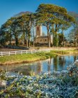 Shanrahan Church, an old church ruins framed by big trees covered in frost in the morning with a river in the foreground; County Tipperary, Ireland — Stock Photo