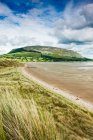 Costa irlandesa com grama de praia e maré retrocedida, com uma montanha planalto e falésias em segundo plano durante o verão; Strandhill, County Sligo, Irlanda — Fotografia de Stock