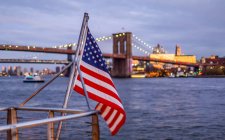 Bandera Americana ondeando desde una barandilla en el paseo marítimo con vistas al Puente de Brooklyn, Manhattan; Nueva York, Nueva York, Estados Unidos de América - foto de stock