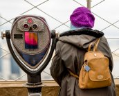 Female tourist standing beside binoculars outside on the observation deck at the Empire State Building in Midtown Manhattan; New York City, New York, United States of America — Stock Photo