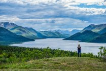Женщина стоит и смотрит на озеро и обширные Юконские хребты; Уайтхорс, Юкон, Канада — стоковое фото