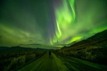 Woman standing on the Dempster Highway under the Northern Lights; Yukon, Canada — Stock Photo