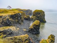 Rugged coastline of the Snaefellsnes Peninsula with a lone house along the cliffs in the mist; Snaefellsbaer, Western Region, Iceland — Stock Photo