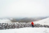 Senderista que mira hacia fuera sobre una vieja pared de piedra en la cima de las montañas Galty en invierno en tiempo nublado y brumoso; Condado de Tipperary, Irlanda - foto de stock