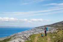 Caminhadas de mulher e cachorro em trilha no Burren olhando para o mar em um dia ensolarado de verão; Fanore, County Clare, Irlanda — Fotografia de Stock