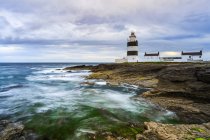 Faro di Hook Head, faro bianco e nero sulla riva rocciosa in una giornata estiva nuvolosa, lunga esposizione; Contea di Waterford, Irlanda — Foto stock