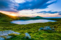 Coucher de soleil sur Lough Muskery dans les Galty Mountains en été avec de grands rochers au premier plan, Galty Mountains ; comté de Limerick, Irlande — Photo de stock