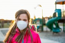 Jeune fille debout sur une aire de jeux portant un masque de protection contre la COVID-19 pendant la pandémie mondiale de coronavirus ; Toronto, Ontario, Canada — Photo de stock