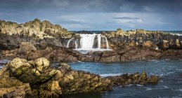 Rugged coastline and water flowing over rocks; Bamburgh, Northumberland, England — Stock Photo