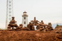Rocks balanced in piles with a lighthouse in the background; Prince Edward Island, Canada — Stock Photo