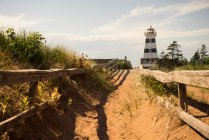 Sandy trail and wooden rail fence leading to a lighthouse on the coast; Prince Edward Island, Canada — Stock Photo