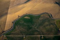 Aerial view of a road winding through farmland divided into green and brown, with an electricity transmission line running across; Colorado, United States of America — Stock Photo