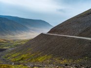 Route contournant un virage sur une colline avec vue sur une vallée et des montagnes sous un ciel couvert ; Westfjords, Islande — Photo de stock