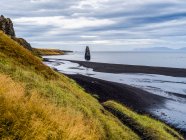 Hohe Felsformationen und grasbewachsene Hänge entlang der Küste eines Fjords; Island — Stockfoto