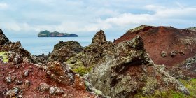 Rugged rock along the coast of the island of Heimaey, with a view of Ellioaey island, a part of an archipelago along the Southern coast of Iceland; Vestmannaeyjar, Southern Region, Iceland - foto de stock