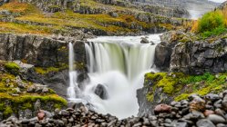 Uma cachoeira sobre uma paisagem rochosa em cores de outono; Djupivogur, Região Leste, Islândia — Fotografia de Stock